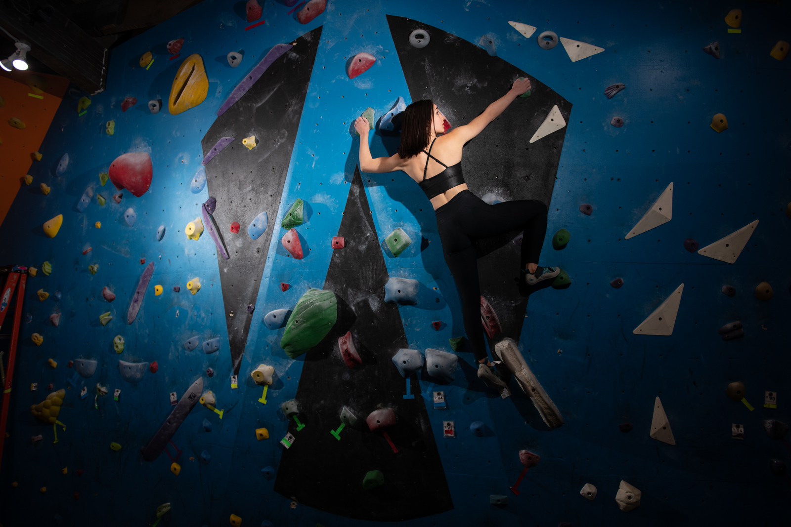 Woman in black athletic wear scaling a colorful indoor bouldering wall, Spokane portrait photography