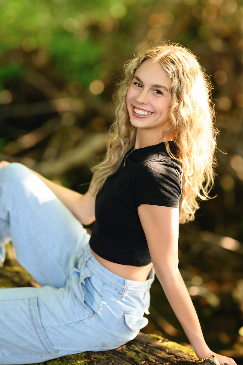 High school senior girl in black crop top and jeans sitting on a mossy log in a Pacific Northwest forest, Spokane senior portraits